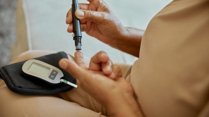 Une personne utilise une lancette pour se piquer le doigt afin d'effectuer un test de glycémie. Un lecteur de glycémie et une bandelette réactive sont placés dans une pochette noire à proximité.